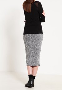 Svart långärmad topp med genomskinliga axlar, matchad med en figurnära gråstickad midiklänning. Modellen har på sig svarta ankelboots.