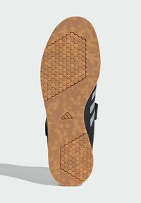 Black shoe sole with a honeycomb pattern in tan rubber. Features a smooth, textured design and three parallel white stripes along the side.