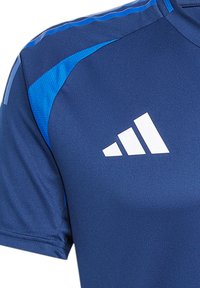 Blauwe sporttshirt met korte mouwen, met gestructureerde schouderpanelen in een lichter blauw en een groot wit Adidas-logo op de borst.