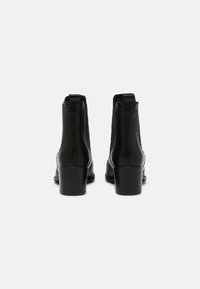 Bottines en cuir noir avec une texture lisse, un bout rond et un talon épais. Elles présentent des détails de couture et des languettes à l'arrière.