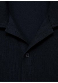 Polo din tricot de culoare bleumarin, cu un material texturat, având un guler pliat și un singur nasture negru la gât.