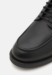 Melnas ādas kurpes ar strukturētu virsmu, apaļu purngalu un kontrastējošām šuvēm. Zole ir plakana, ar vieglu izliekumu.