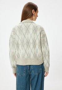 Strickjacke mit einem Rautenmuster in Beige und Hellgrau, mit einem verkürzten Design und geripptem Saum. Das Material wirkt weich und strukturiert.