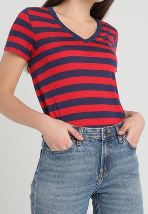 T-shirt a righe rosse e blu con scollatura a V, realizzata in morbido tessuto, abbinata a jeans blu a vita alta.