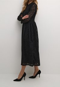 Svart spetsklänning med långa ärmar, en åtsittande överdel och en utställd kjol, med blomm önster, lagerstruktur, i kombination med svarta stiletto skor.