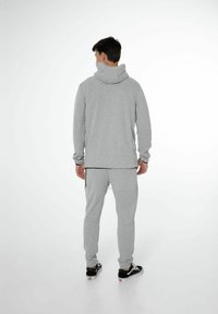 Haut de survêtement en coton gris avec col haut et manches longues, associé à un pantalon de survêtement gris assorti. La tenue présente une coupe décontractée et des poignets côtelés.