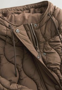 Braune gesteppte Jacke mit Steppmuster, ausgestattet mit Reißverschluss, Kapuze mit Kordelzug und metallischen Druckknöpfen. Weiche Stofftextur.