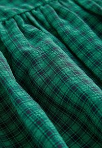 Tessuto a quadri verdi con una trama textured, caratterizzato da un motivo a scacchi in diverse tonalità di verde e nero, creando un aspetto stratificato.