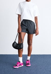 Pantaloncini atletici neri, maglietta bianca, scarpe da ginnastica rosa e nere, e una piccola borsa nera. Calzini bianchi alla caviglia. Design e materiali semplici.