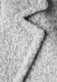 Mjukt grått tyg med en strukturerad, krullig yta. Materialet verkar frodigt, med tätt rullade fibrer och en något fluffig finish.