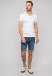 T-shirt en coton blanc à col en V associé à un short en denim bleu, retroussé au niveau de l'ourlet, et des chaussures à enfiler beige clair. Design simple et coupe décontractée.