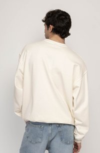 Hanorac supradimensionat de culoare crem, realizat dintr-un material moale, cu un croi lejer și mâneci largi, purtat cu blugi din denim de culoare albastru deschis.