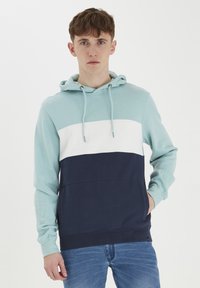 Hooded majica s tri boje bloka: svijetlo plava, bijela i tamnoplava. Izrađena od mekog materijala, s kengur džepom i kapuljačom s uvećanom vrpcom.