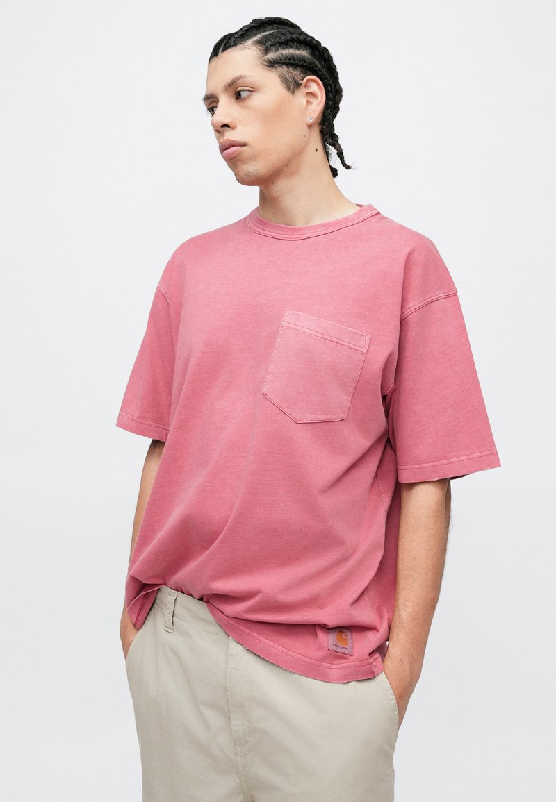 Rosa oversized t-shirt med rund hals og brystlomme. Stoffet virker blødt og let tekstureret. Bruges med lyse beige shorts.