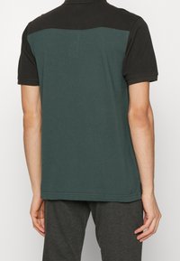 Pánská polo košile s černým límečkem a zadním dílem, s tmavě zeleným spodním dílem. Krátké rukávy, hladká textura a ležérní střih.