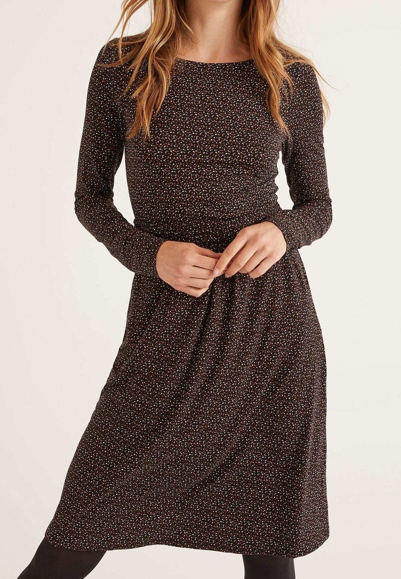 Robe à manches longues en tissu foncé avec de petits pois multicolores. Elle est dotée d'un corsage ajusté et d'une jupe fluide. Texture douce.