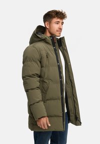 Chaqueta de plumas de color verde oliva con capucha, que cuenta con un cierre zip, dos bolsillos laterales y un bolsillo en el pecho. Material texturizado con detalles de costura.