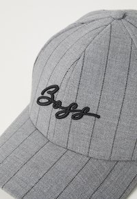 Grau angemützte Kappe mit vertikalen Nadelstreifen, die ein schwarzes gesticktes Logo zeigt. Das Material wirkt strukturiert, mit einem gebogenen Schirm und genähten Akzenten.