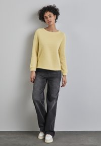 Maglione giallo, strutturato, con maniche lunghe e scollatura rotonda abbinato a jeans dritti grigi e sneakers bianche.