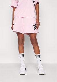 Conjunto deportivo rosa que incluye una camiseta holgada y pantalones cortos a juego con rayas negras. Combinado con zapatillas blancas y calcetines a rayas.