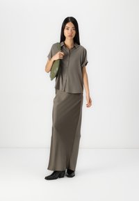 Camicia verde oliva a maniche corte con bottoni abbinata a una lunga gonna aderente verde oliva e stivaletti neri con tacco; design elegante e minimalista.