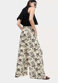 Wijdvallende broek van crèmekleurige stof met een zwart bloemenpatroon. Elastische tailleband, zijzakken en een relaxte pasvorm.