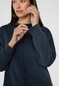 Granatowy sweter z okrągłym dekoltem i długimi rękawami. Tkanina ma gładką teksturę i charakteryzuje się delikatnym szwem z przodu.