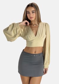 Beige kort topp med plisserad design och ballongslevar, ihop med en grå minikjol med bälte och enkel spänndetalj.