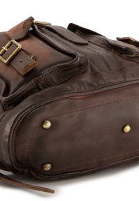 Bruine leren rugzak met messing beslag, meerdere buitenzakken en een gestructureerde afwerking. Voorzien van stiksels en klinknagels voor extra duurzaamheid.