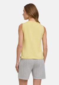 Mouwloos geel topje, textuurstof, geribbelde halslijn, gecombineerd met lichtgrijze shorts met verticale strepen. Minimalistisch ontwerp, casual pasvorm.