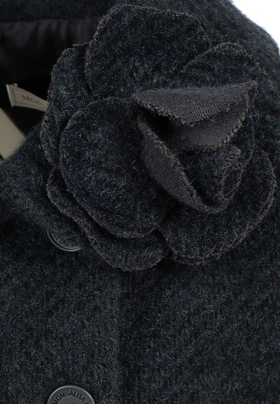 Cappotto in lana nera, testurizzato, con un accento floreale rotondo al colletto e chiusura con bottone. Presenta dettagli fini e una finitura morbida.