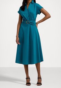 Teal klänning i slätt tyg; har krage, korta ärmar och en åtsittande midja med en dekorativ spänne. Mittenlång, utsvängd kjol.