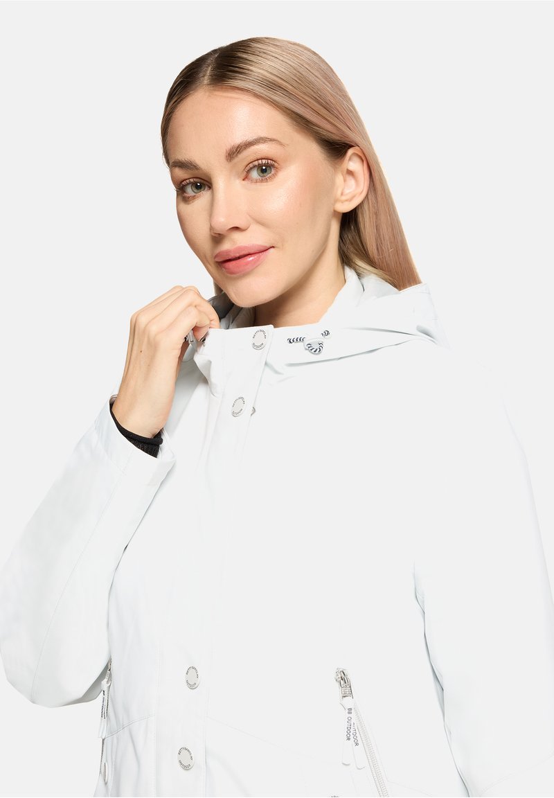 Veste blanche imperméable avec capuche, équipée de pièces métalliques argentées, poches zippées et texture lisse. Détails comprennent un cordon de serrage pour l'ajustement.