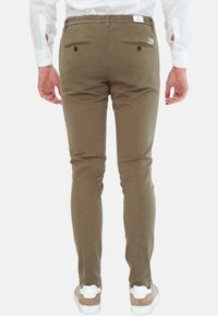 Pantaloni aderenti verde oliva con una texture liscia, due tasche posteriori con chiusura a bottoni, indossati con sneakers bianche.
