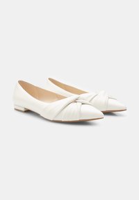 Ballerines blanches en cuir avec un bout pointu et un détail de nœud tordu à l'avant. Elles ont un petit talon et une texture lisse.