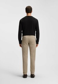 Maglietta nera a maniche lunghe e pantaloni beige chiaro. Tasche posteriori in stile giacca. Texture liscia, vestibilità casual e dettagli minimi.