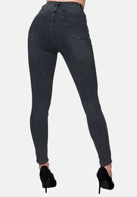 Jeans de mezclilla negra ajustada con cintura alta, bolsillos traseros y una silueta entallada, combinados con zapatos de tacón alto negros.