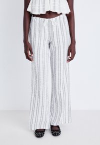 Pantalons en lin blancs à rayures avec une taille élastique et un cordon de serrage. Accentués de rayures bleu clair. Silhouette à jambes larges. Chaussures plates noires.