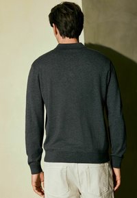 Dunkelgrauer Langarmpullover mit einem gerippten Kragen und Bündchen, ausgestattet mit einer glatten Textur und einem enganliegenden Design. Rückansicht, schlichte Rückseite.