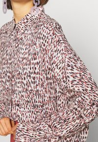Blusa de manga larga en tejido ligero con un patrón abstracto en tonos rosa y negro, con un cuello clásico y un corte holgado.