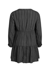 Musta mekko, jossa on pystysuorat raidat, pitkät hihat ja kerroksellinen helma. Valmistettu teksturoidusta kankaasta, jossa on joustava vyötärö rauhallista istuvuutta varten.