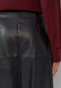 Zwarte leren rok met een gladde textuur, voorzien van een naaddetail. Gecombineerd met een kastanjebruine trui, zichtbaar geribde manchetten.