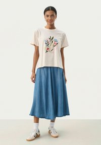 T-shirt crème à manches courtes avec un imprimé floral. Associé à une longue jupe en denim avec des poches latérales. Chaussures : baskets blanches avec des accents.