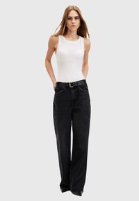 Witte mouwloze top gecombineerd met hoge taille zwarte wijde-leg jeans. De jeans hebben een gestructureerde afwerking en een zwarte riem met een gouden gesp.
