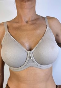 Sostén beige con un diseño texturizado, copas moldeadas y tirantes ajustables. Presenta un cierre decorativo en la parte frontal.