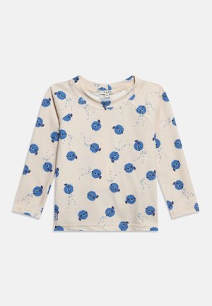 Beež värvusega pikkade varrukatega väikelapse särk, millel on kõikjal siniste kärbsepüügikalade mustriga ja väikesed mullid, ümar kaelus ning nähtav brändi silt.