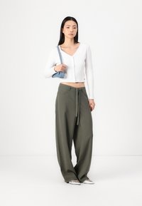 Haut à manches longues blanc à côtes avec des boutons, associé à un pantalon ample vert olive avec une taille à nouer. Accessoire : petit sac à main bleu. Chaussures argentées.