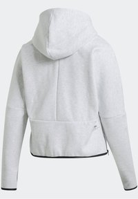 Veste à capuche gris clair avec manches longues, détails de fermeture éclair noirs sur les côtés et ourlet légèrement élastique à l'arrière.