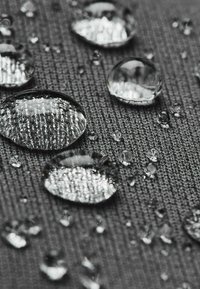 Water droplets on textured gray fabric, showcasing a tight weave pattern. The droplets vary in size, reflecting light and surface details.