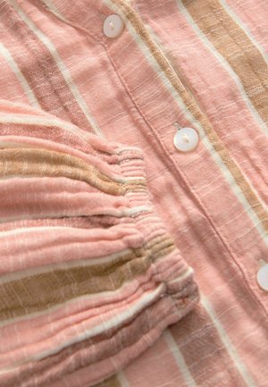 Gestreifter Stoff in Rosa und Beige mit einer strukturierten Oberfläche, weißen Knöpfen, gerafften Ärmelabschlüssen und einem leicht zerknitterten Aussehen.